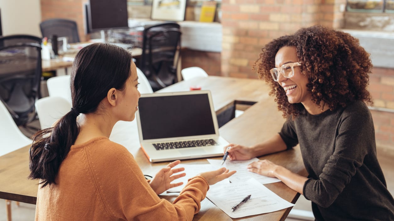 Two women talking at a table in an office.