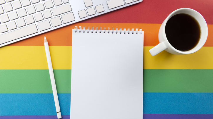 A blank notepad with a cup of coffee and a keyboard on a rainbow colored background.