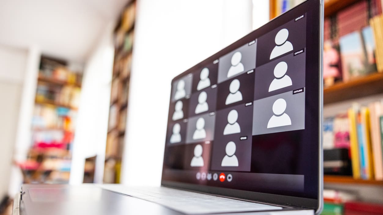 A laptop with people on it in front of a bookshelf.