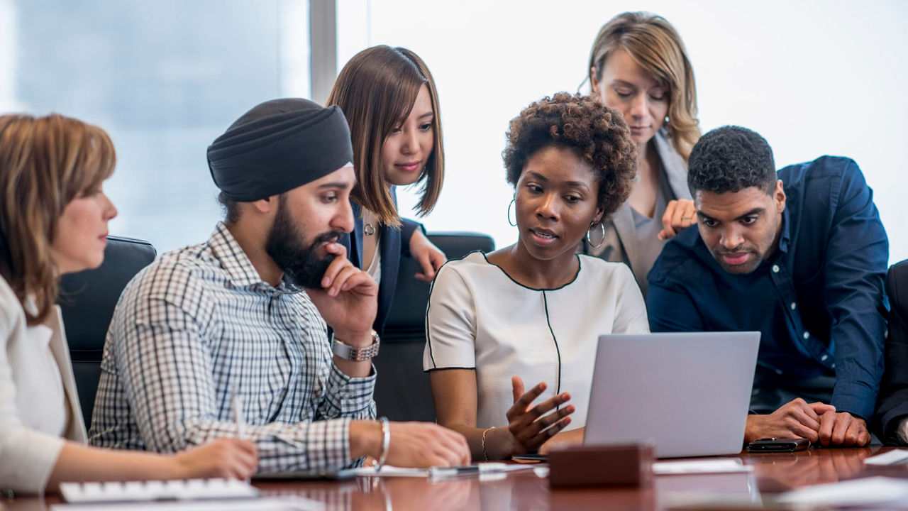 A group of business people looking at a laptop in a conference room.