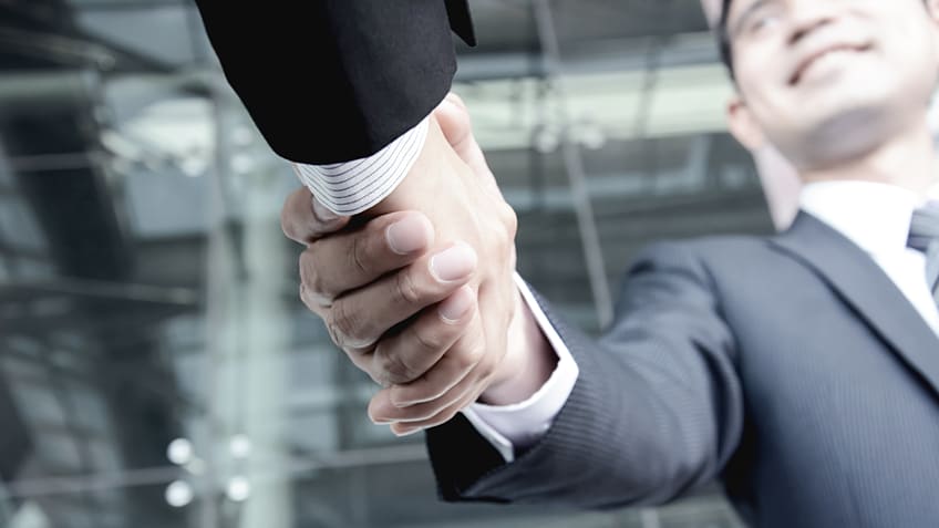 Two businessmen shaking hands in front of a building.