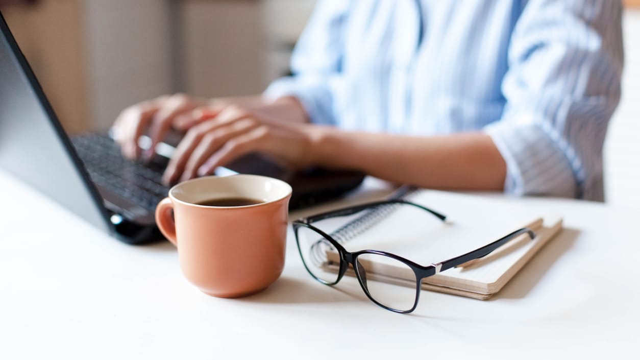 A woman working on a laptop with glasses and a cup of coffee.