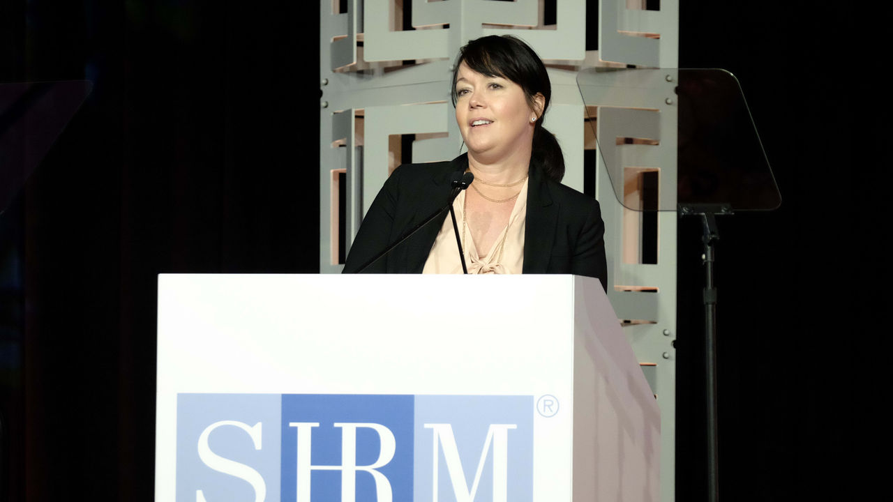 A woman speaking at a podium with the srm logo.