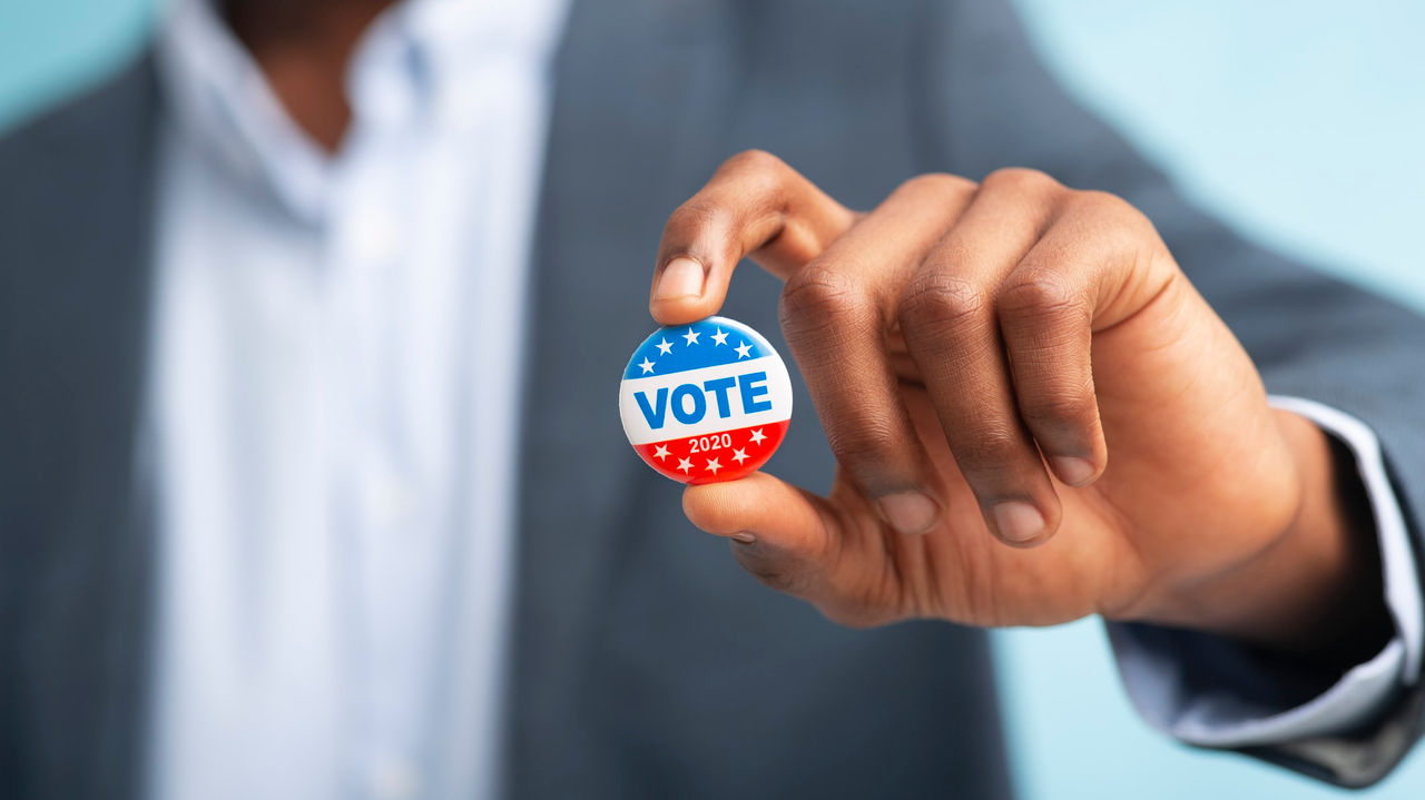 A man holding a button with the word vote on it.