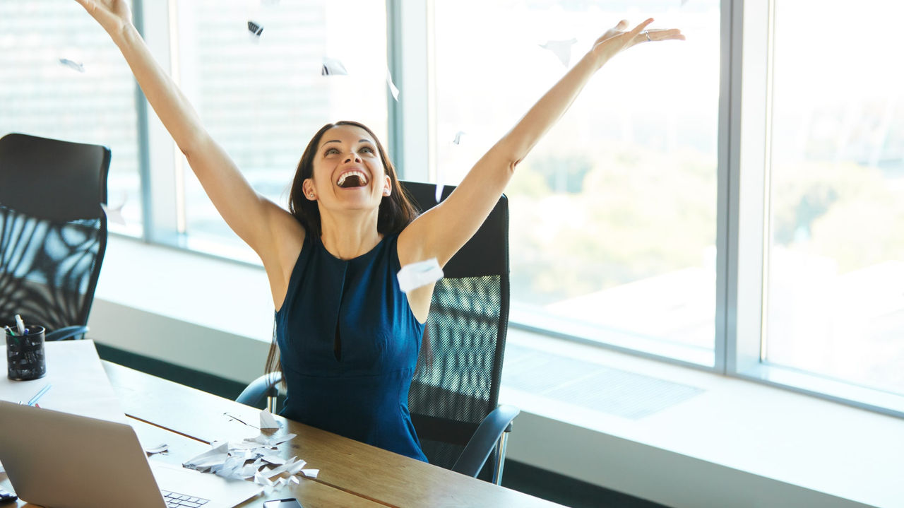 A woman with her arms raised in the air in an office.