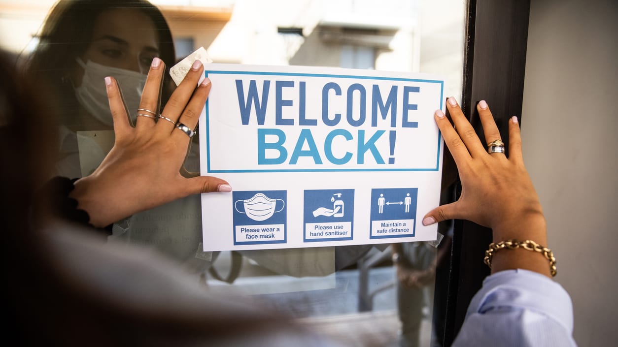 A woman holding a welcome back sign in front of a door.