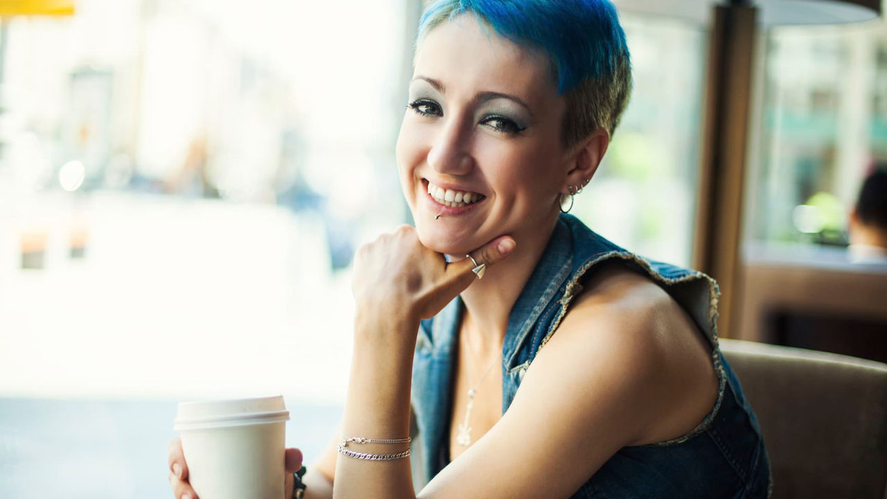 A woman with blue hair holding a cup of coffee.