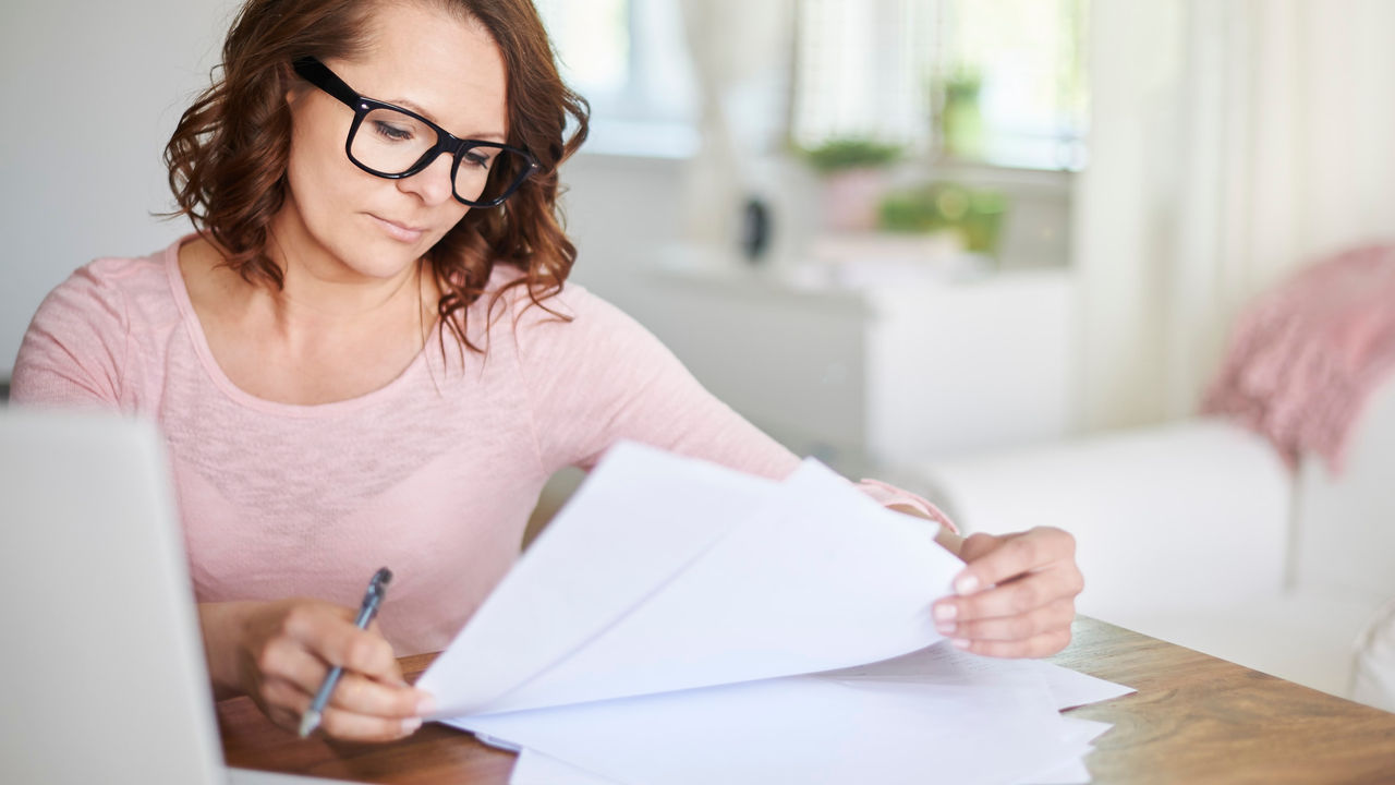 A woman sitting at a table with papers and a laptop.