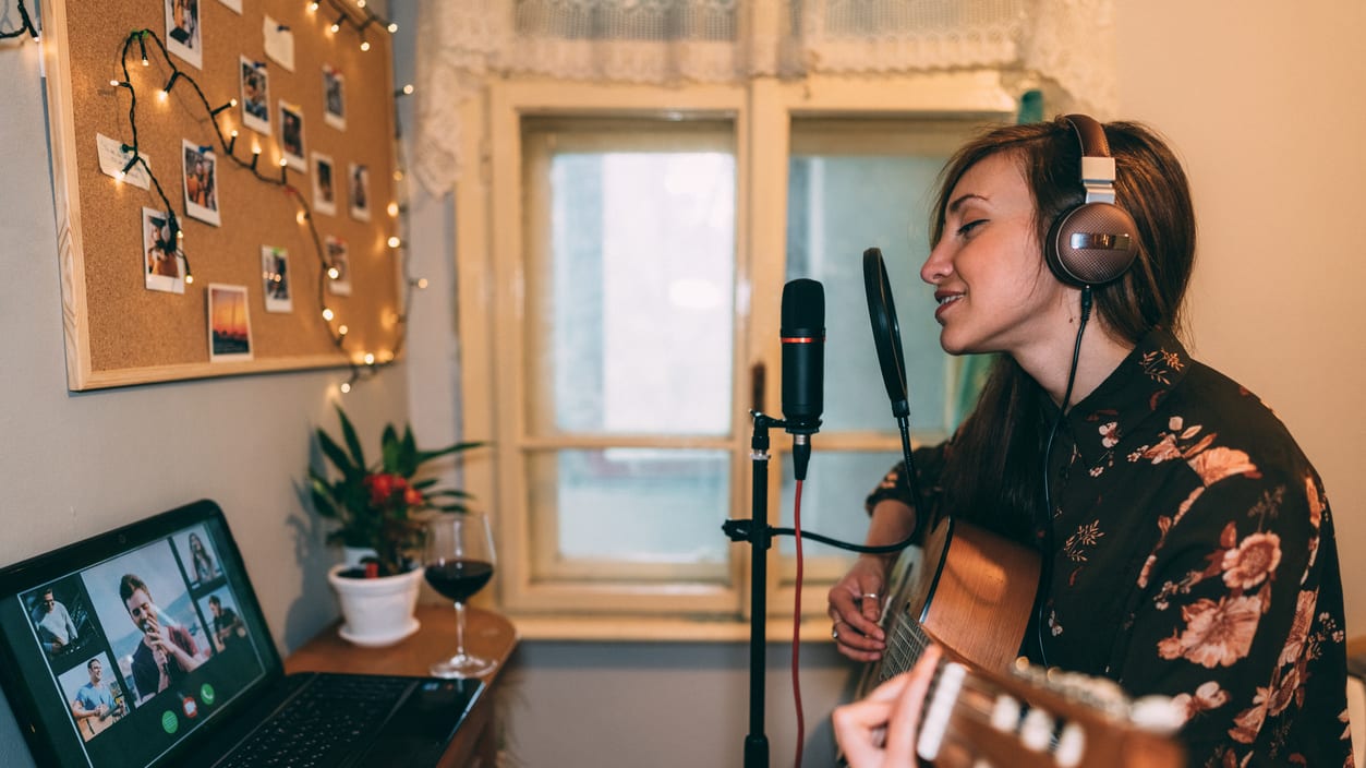 A girl playing an acoustic guitar in front of a laptop.