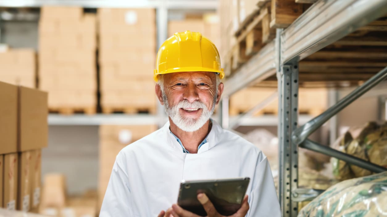 A man in a hard hat using a tablet in a warehouse.
