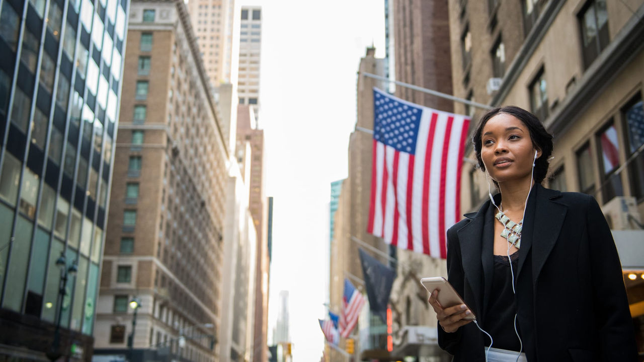 A young african american woman in a business suit walking down a city street with an american flag.