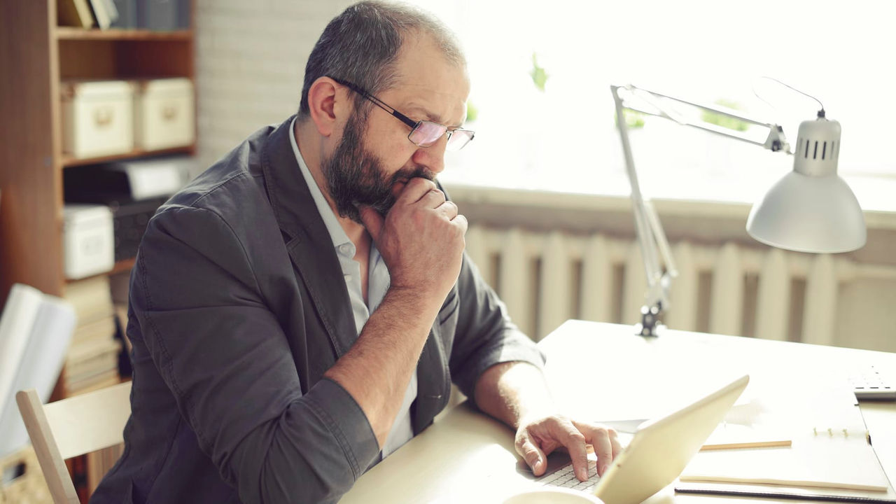 A man sitting at a desk looking at his laptop.