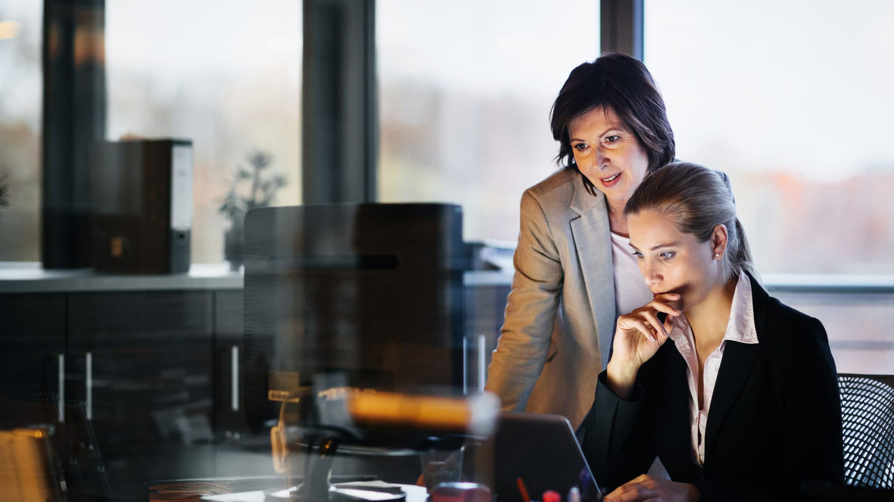 Two business women looking at a laptop in an office.