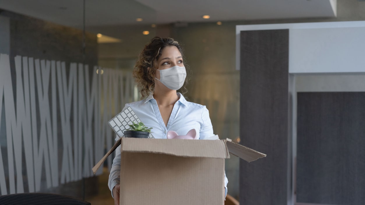 A woman wearing a face mask is carrying a box in an office.