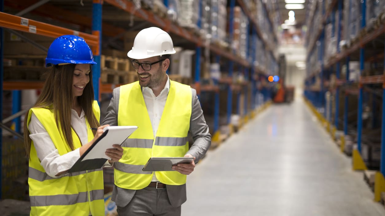 Two people in hard hats standing in a warehouse.