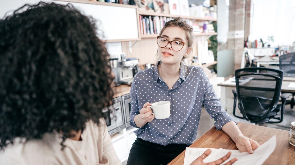 Two women talking at a table in an office.