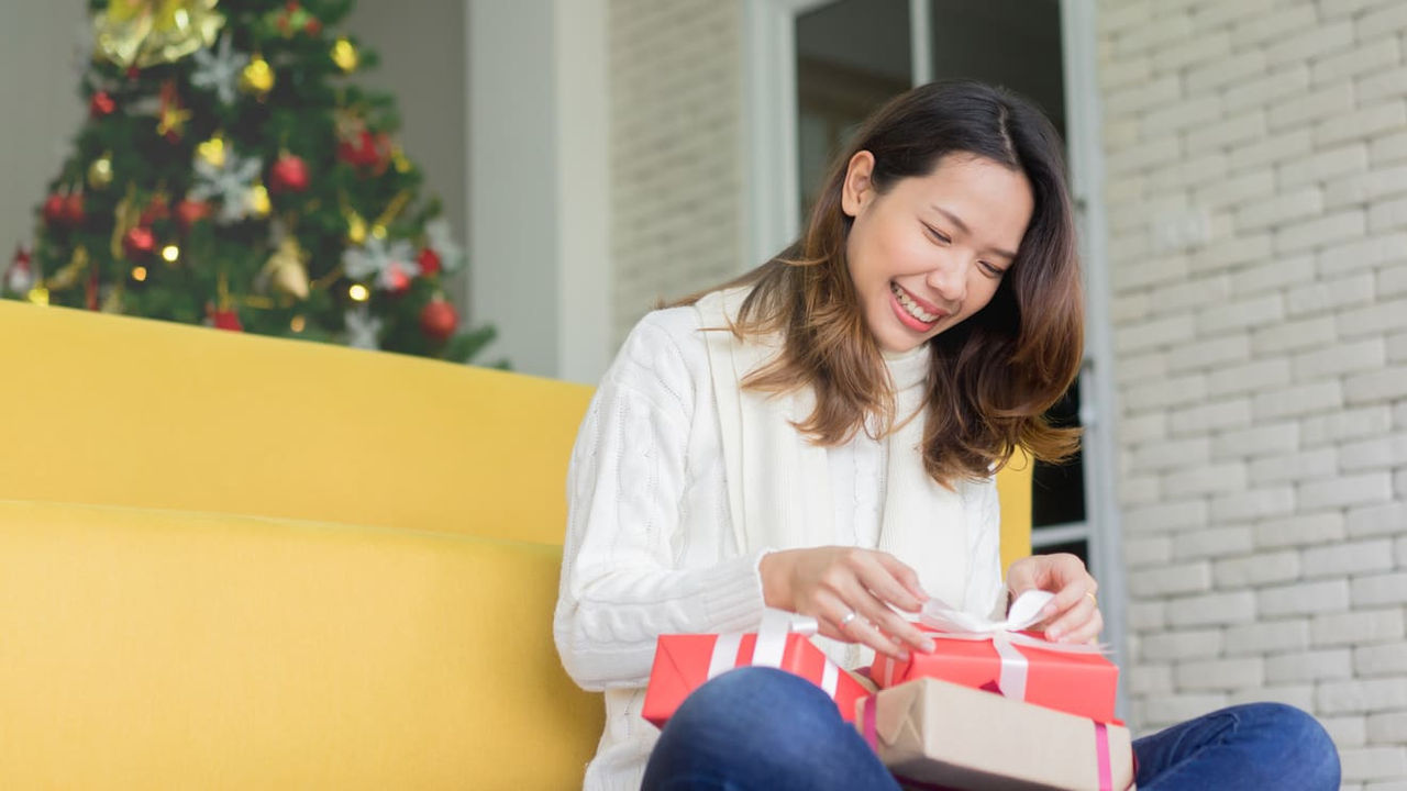 woman opening a christmas present in front of a christmas tree.