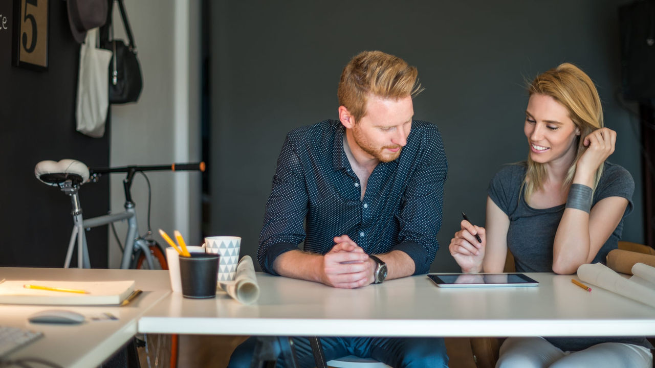 A man and woman sitting at a table looking at a tablet.