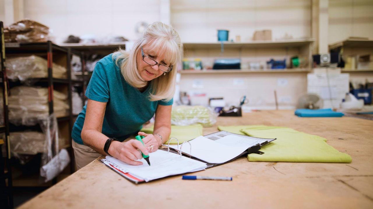 A woman writing on a notebook in a workshop.