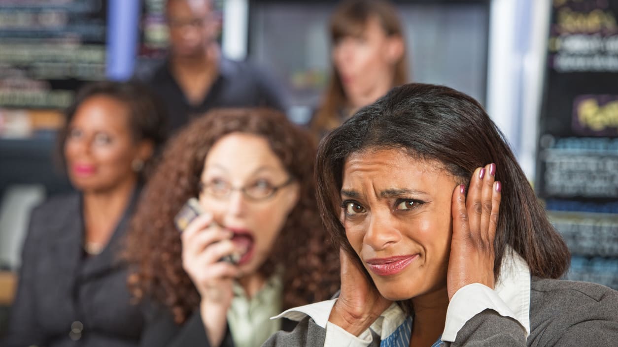 A group of women in a restaurant with their hands on their ears.