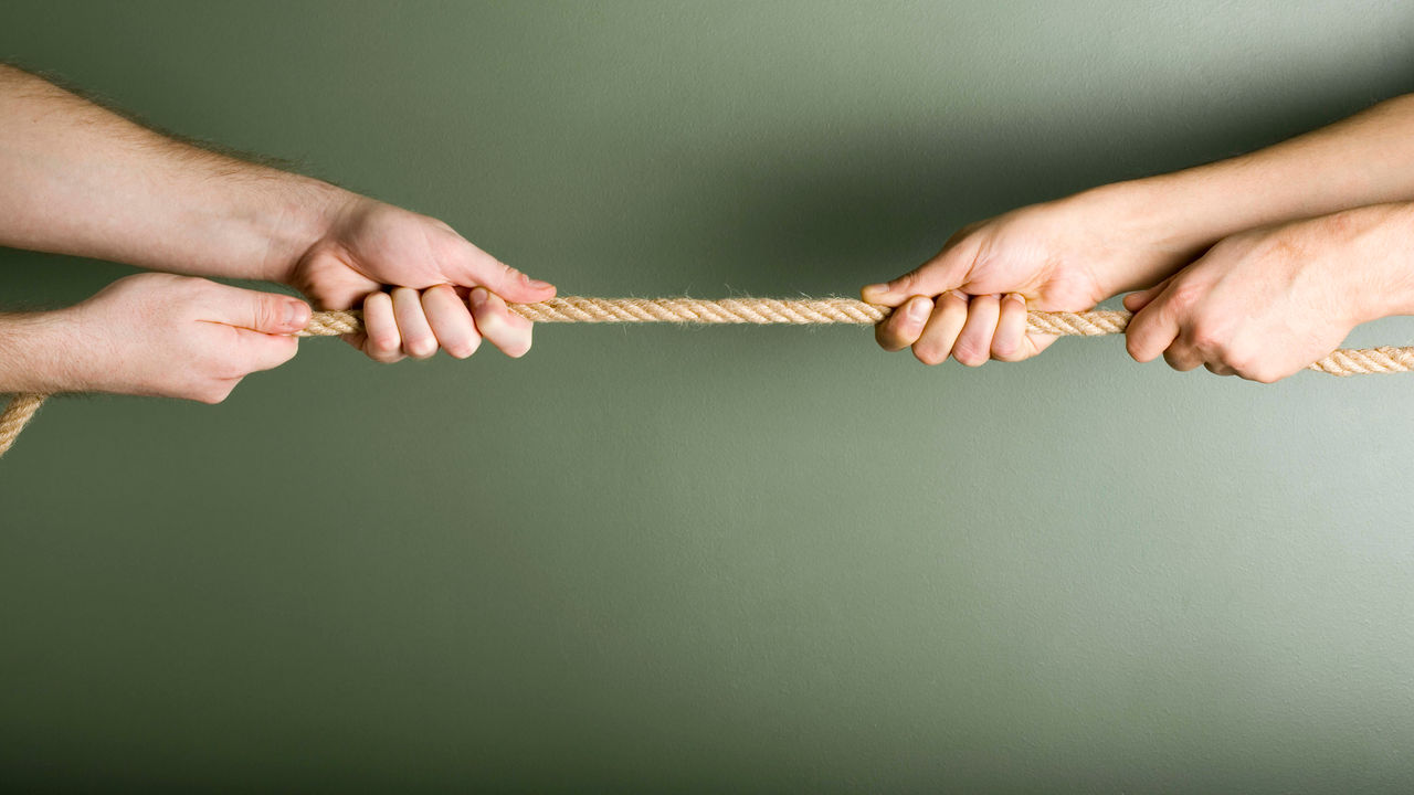 Two hands pulling a rope on a green background.