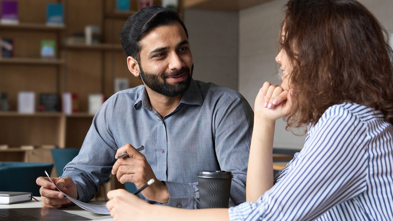 Two employees, a man and a woman, talking to each other at work
