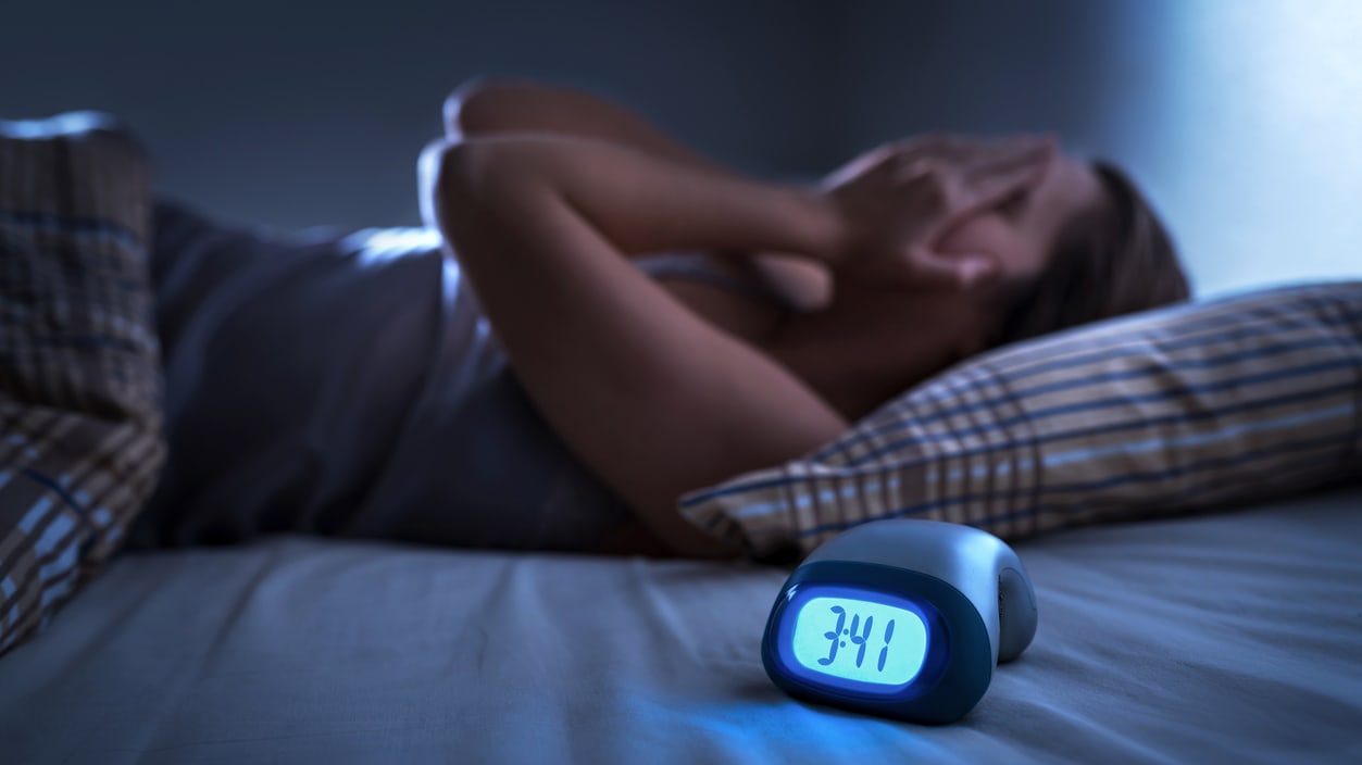 A woman laying in bed with an alarm clock.