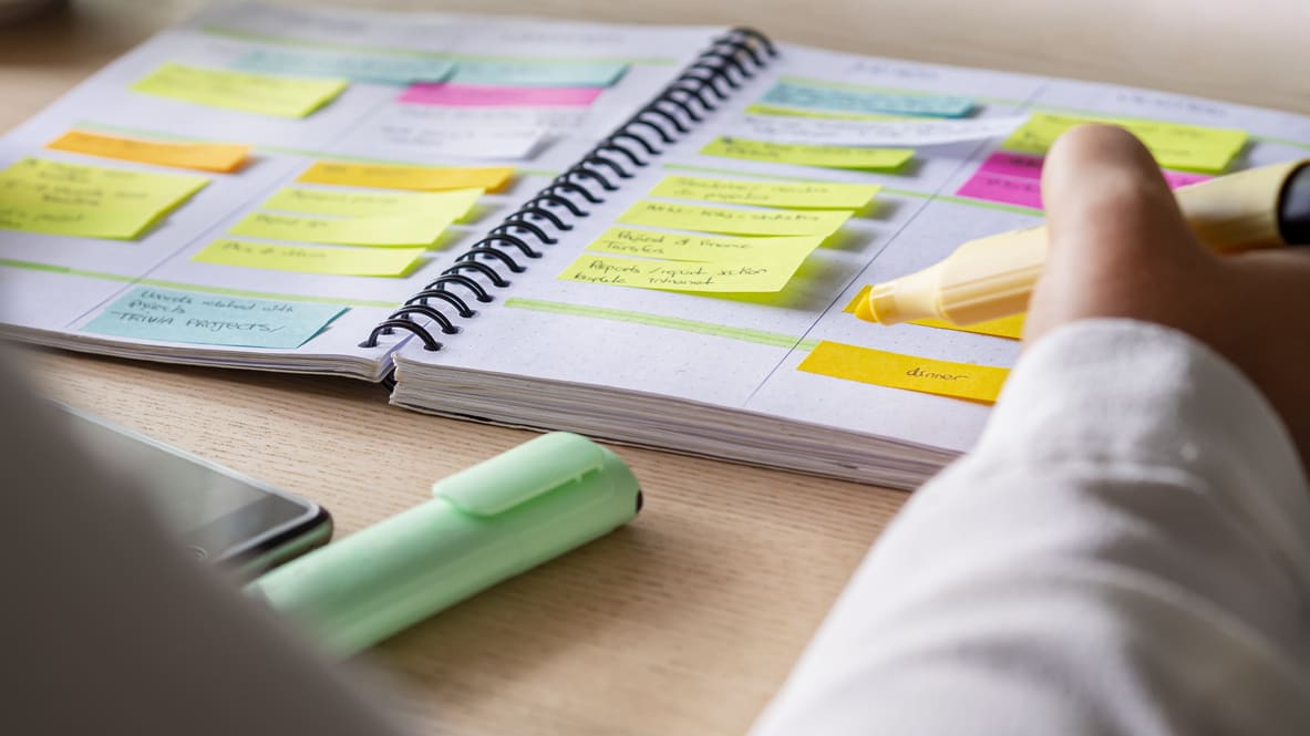 A person writing on a notebook with sticky notes.