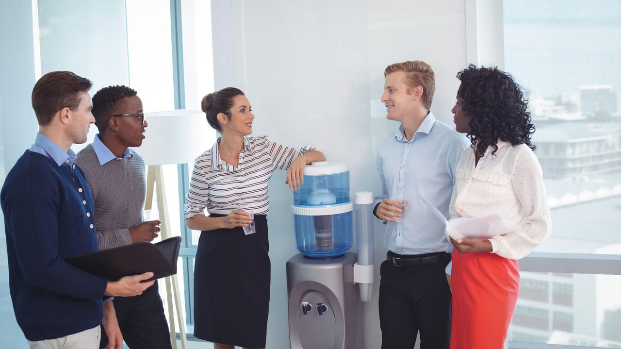 A group of people standing around a water dispenser in an office.