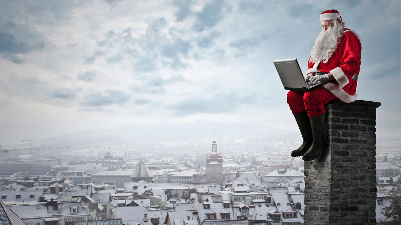 Santa claus sitting on top of a chimney with a laptop.