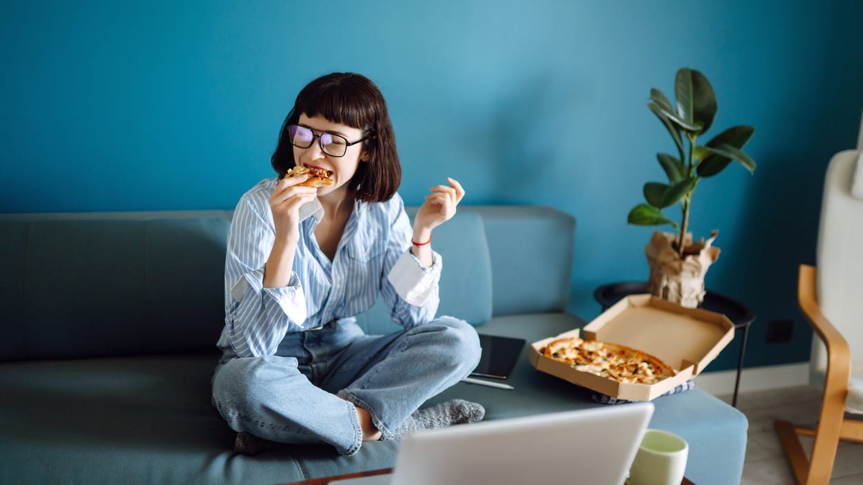 A woman sitting on a couch eating pizza.