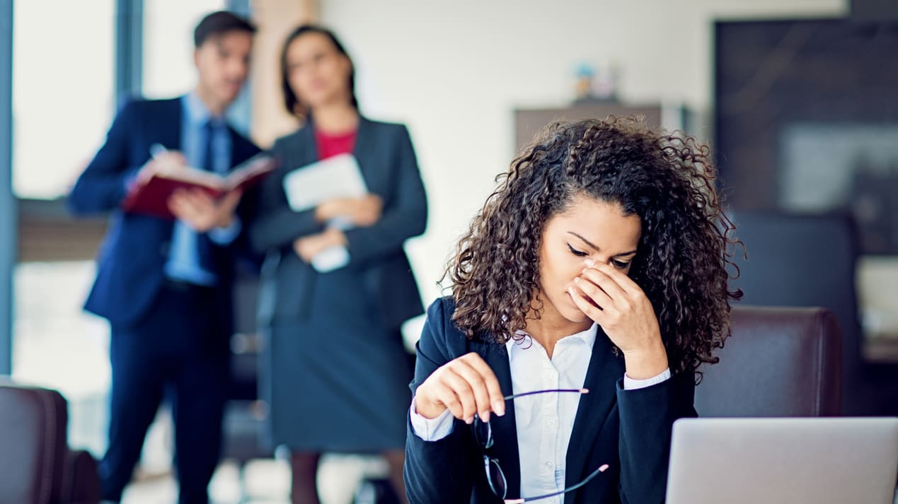 A woman in a business suit is covering her eyes while sitting at a desk.