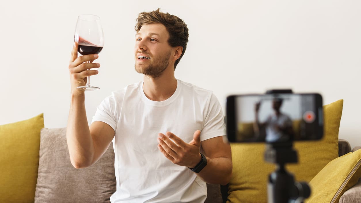 A man is holding a glass of wine while holding a video camera.