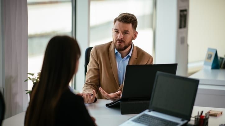 A man and woman talking at a desk in an office.