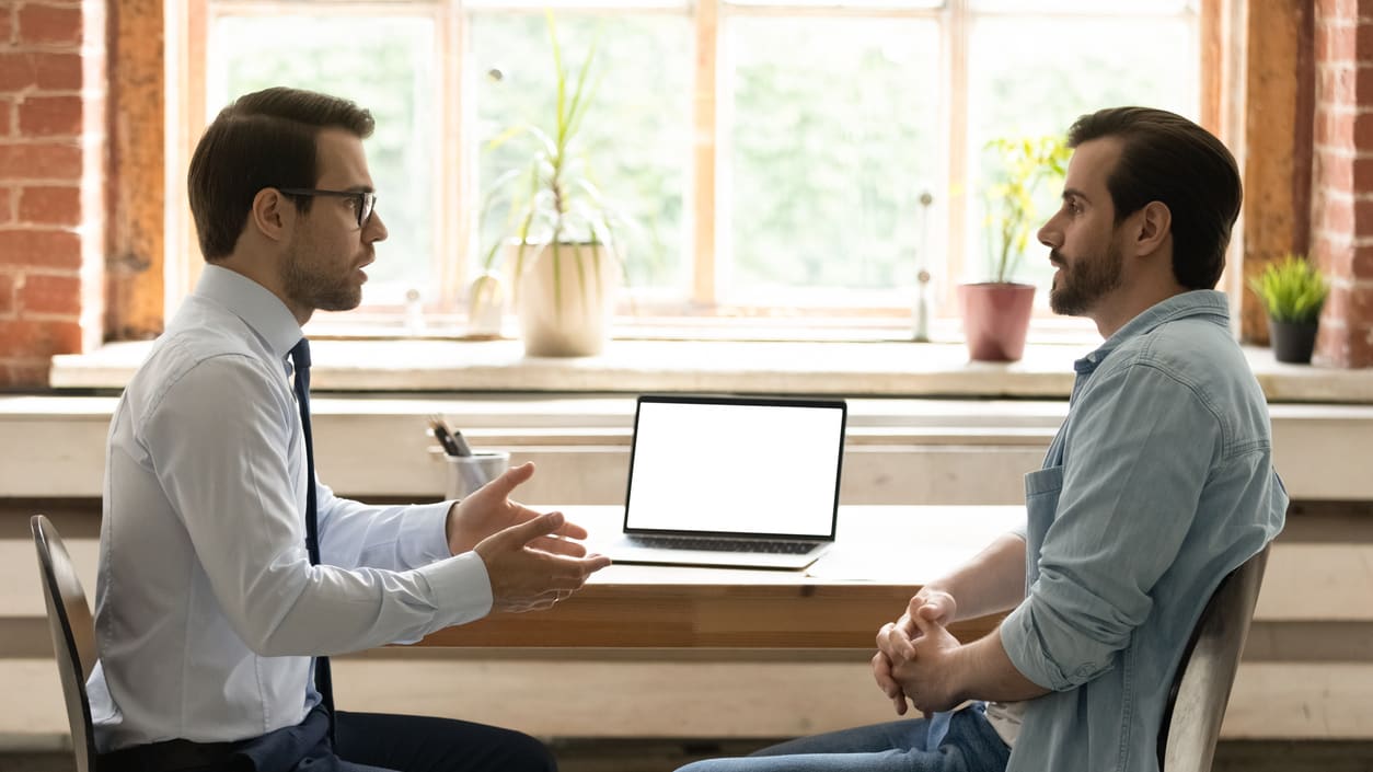 Two men sitting at a table talking to each other.