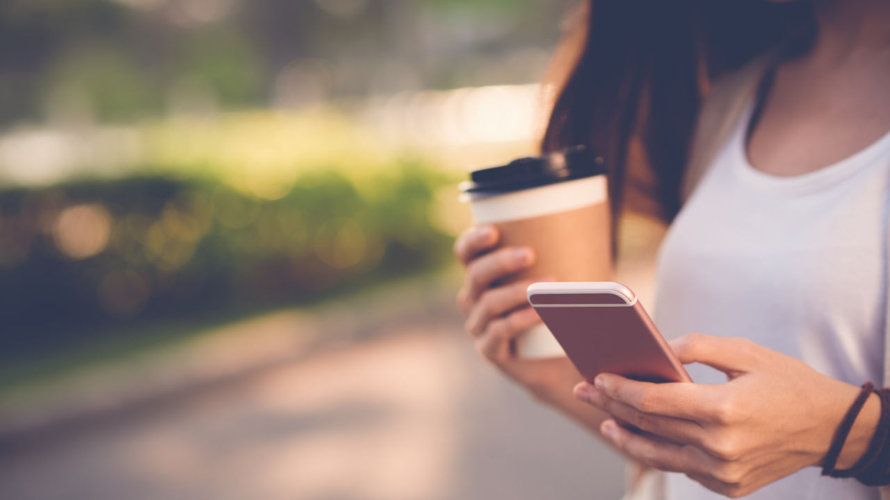 A woman holding a cup of coffee and a cell phone.