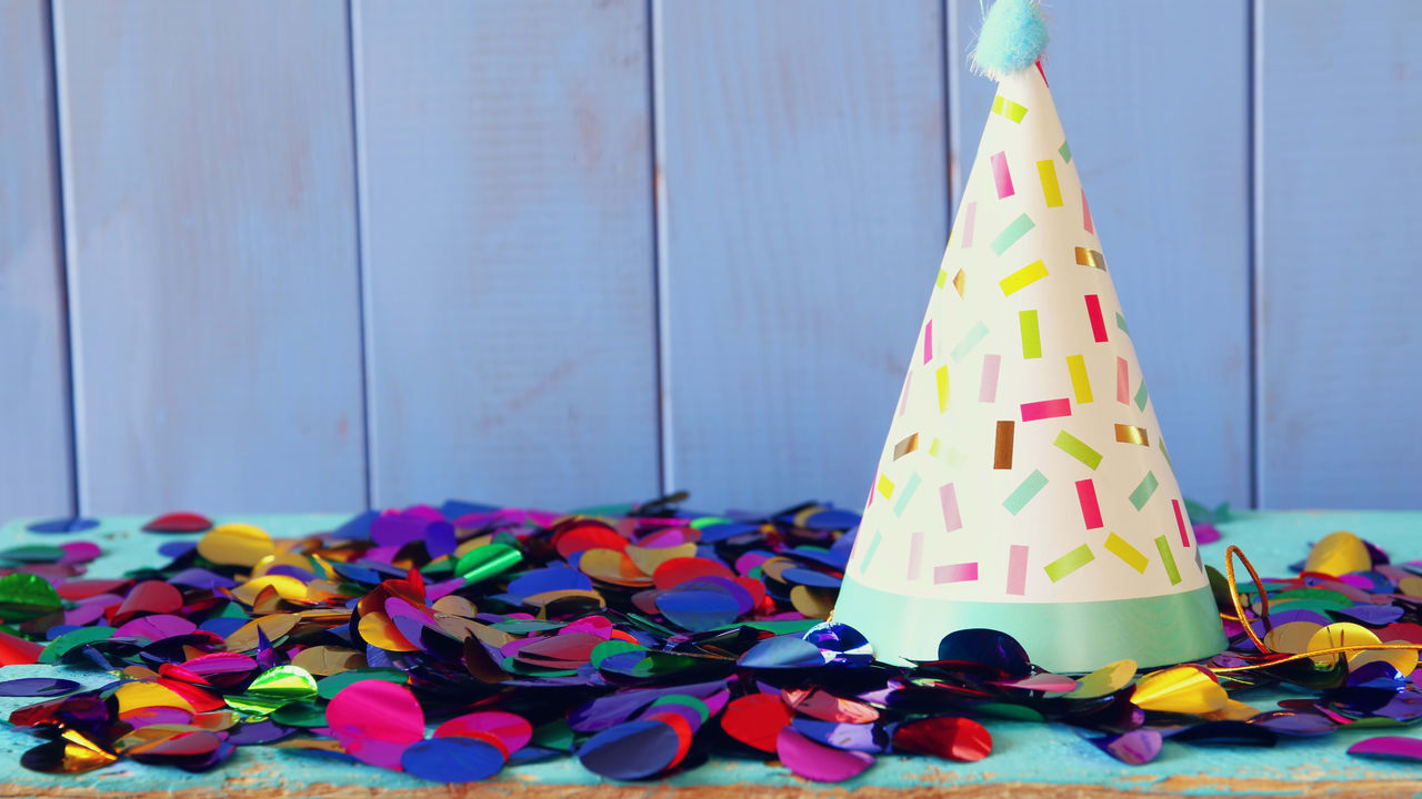 A party hat with colorful confetti on a blue background.