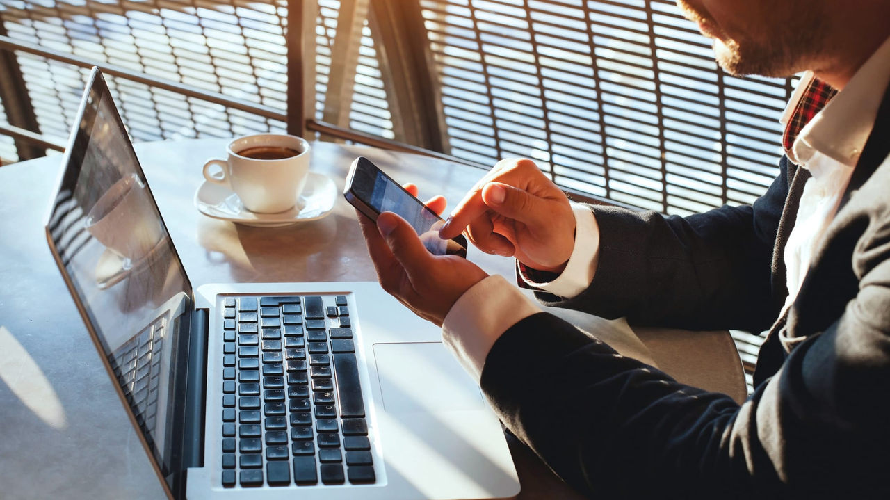 A man in a suit sitting at a table with a laptop and cell phone.