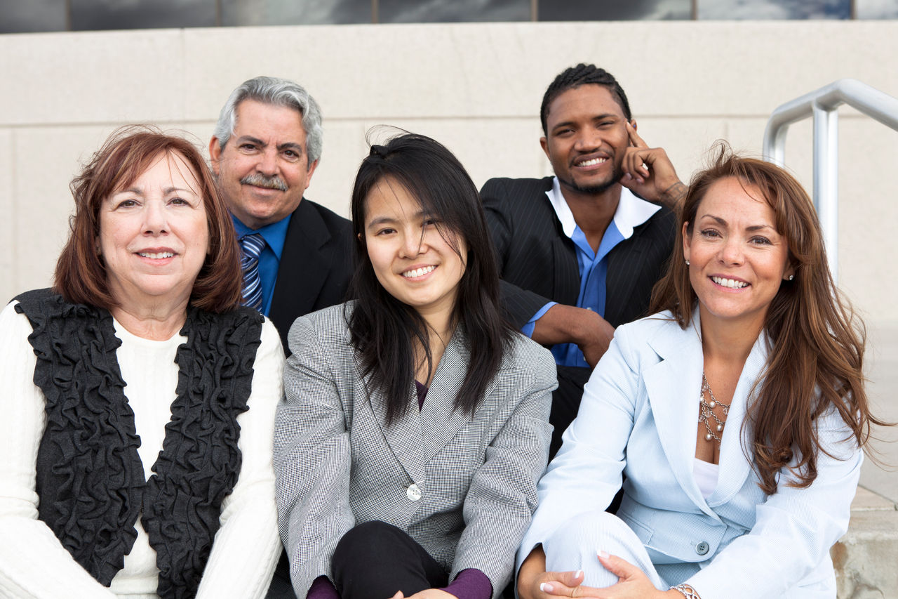 Multigenerational group of people sitting outdoors, smiling and looking at the camera.