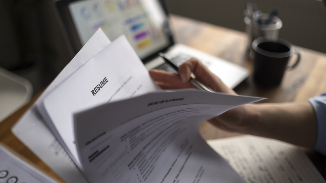 A person writing a resume in front of a laptop.