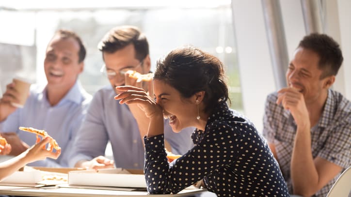 A group of people laughing at a table while eating pizza.