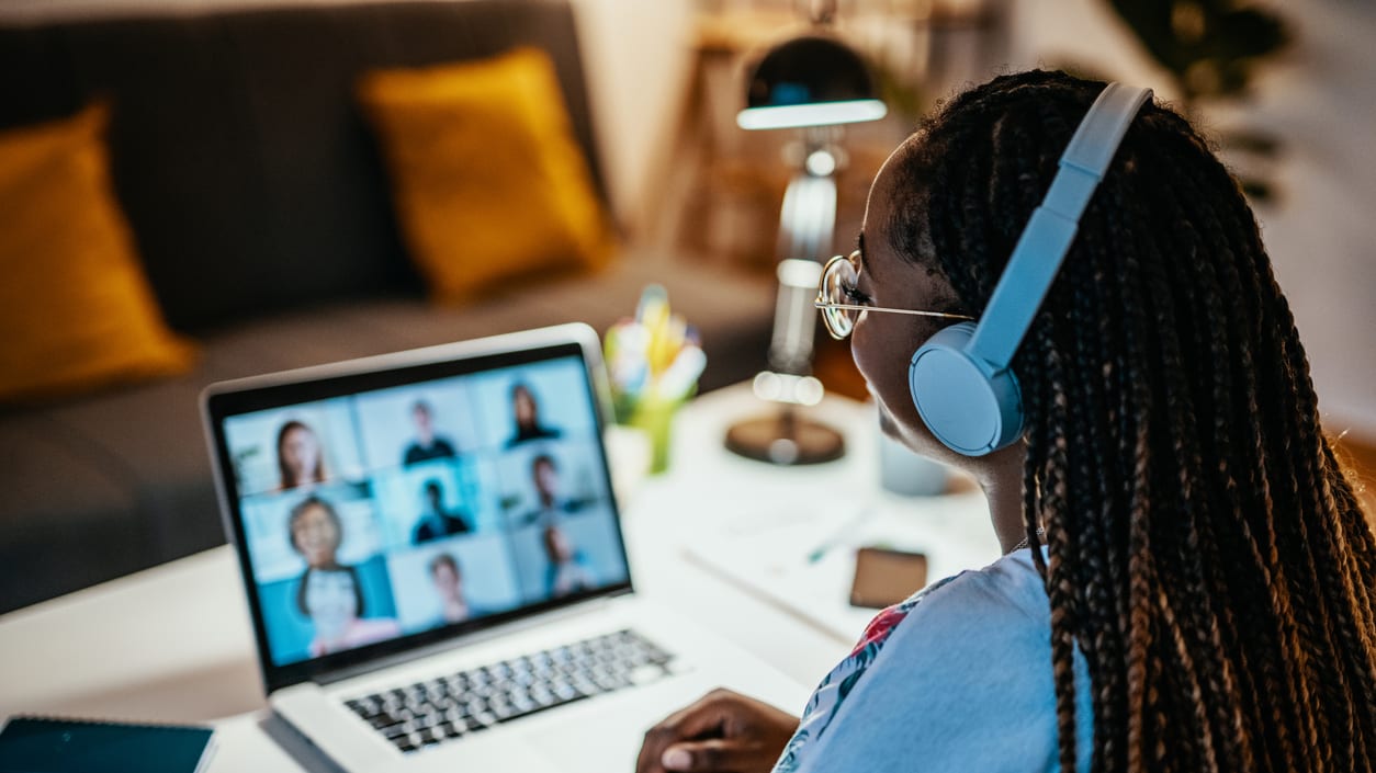 A woman wearing headphones is using a laptop with a video call on it.