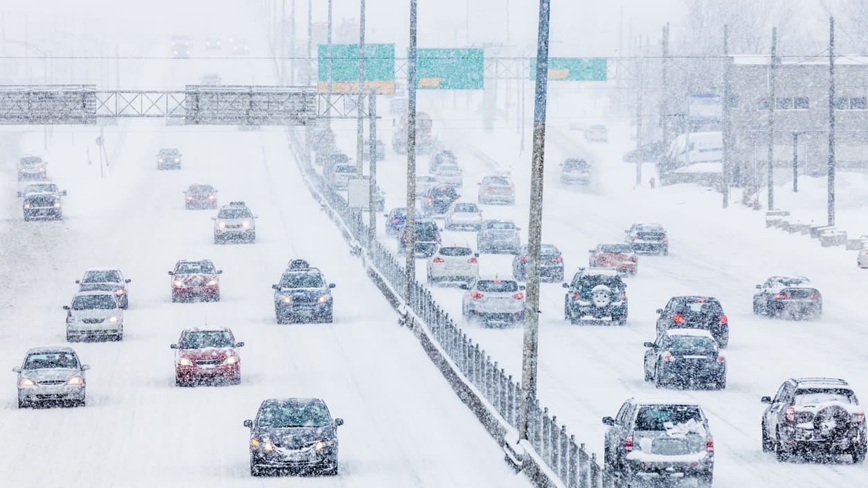 A group of cars driving down a snow covered highway.