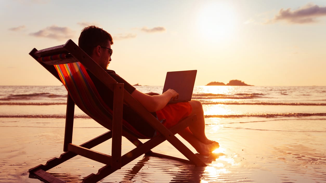 A man sitting in a beach chair with a laptop.