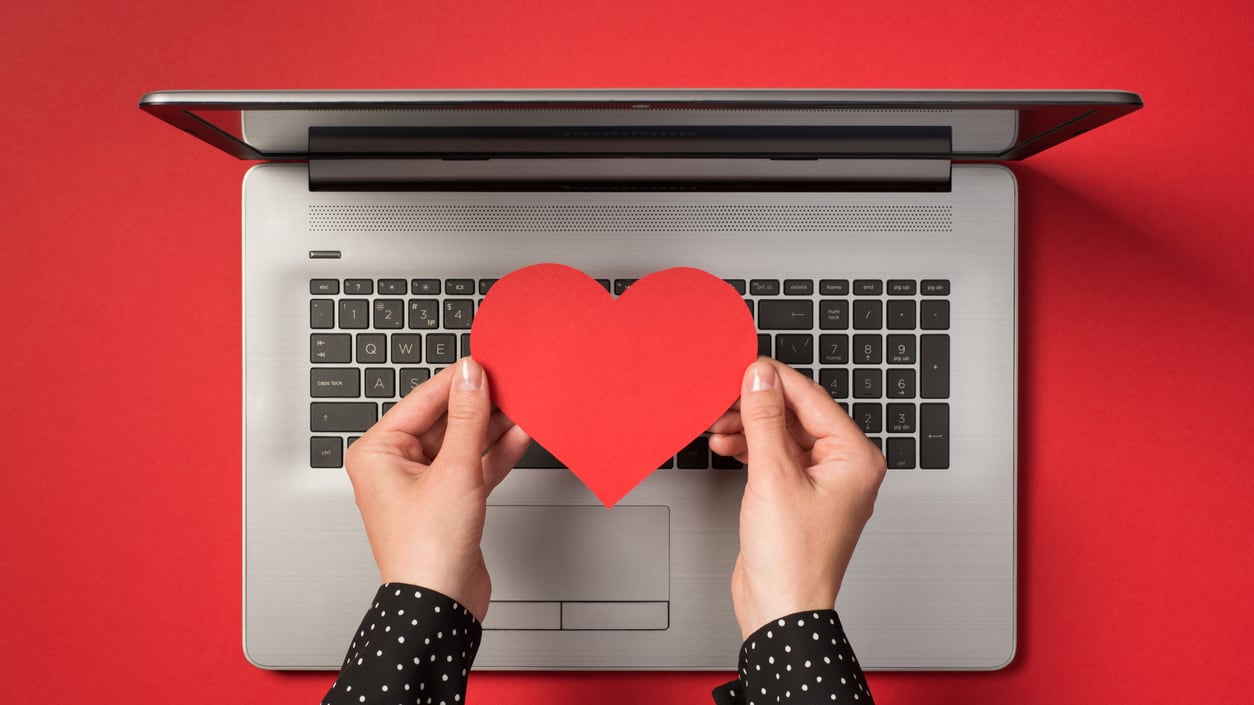 A woman's hands holding a red heart on a laptop.