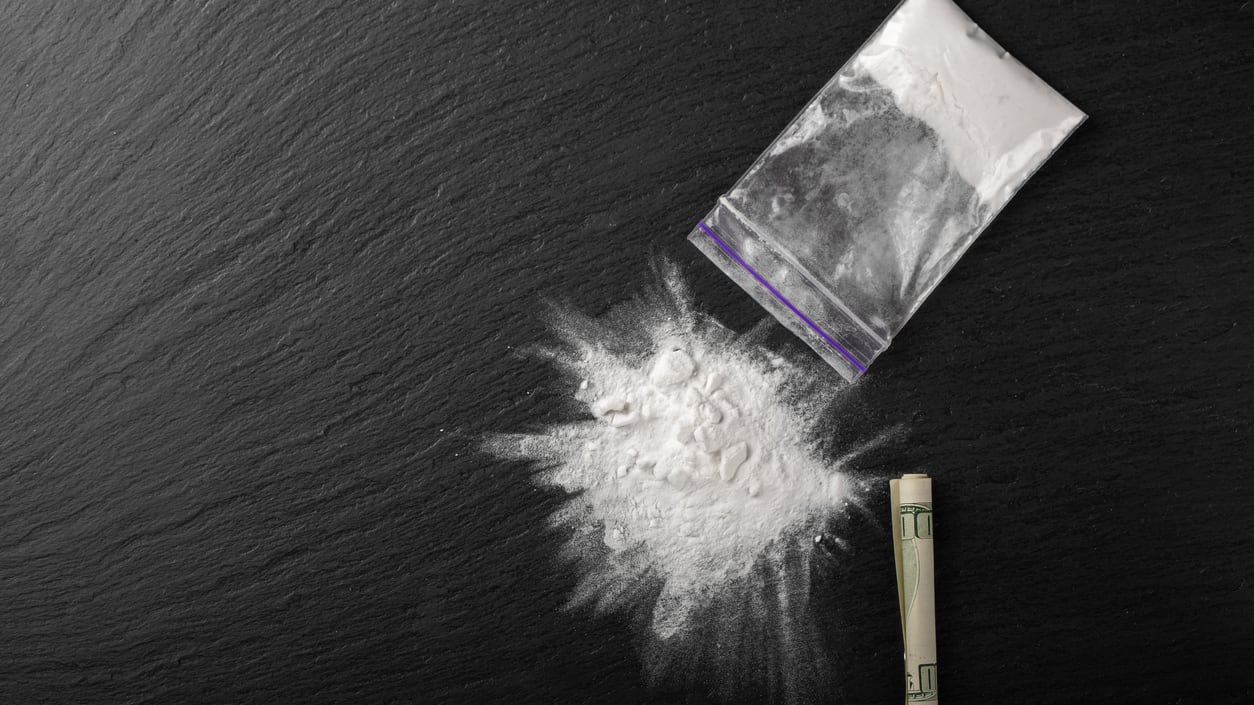 A bag of white powder and a cigarette on a black background.