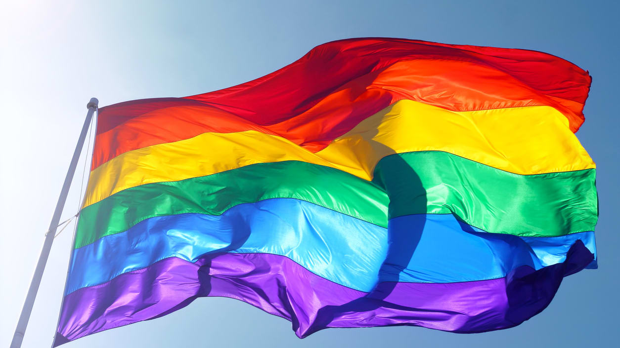 A rainbow flag flies in the wind.