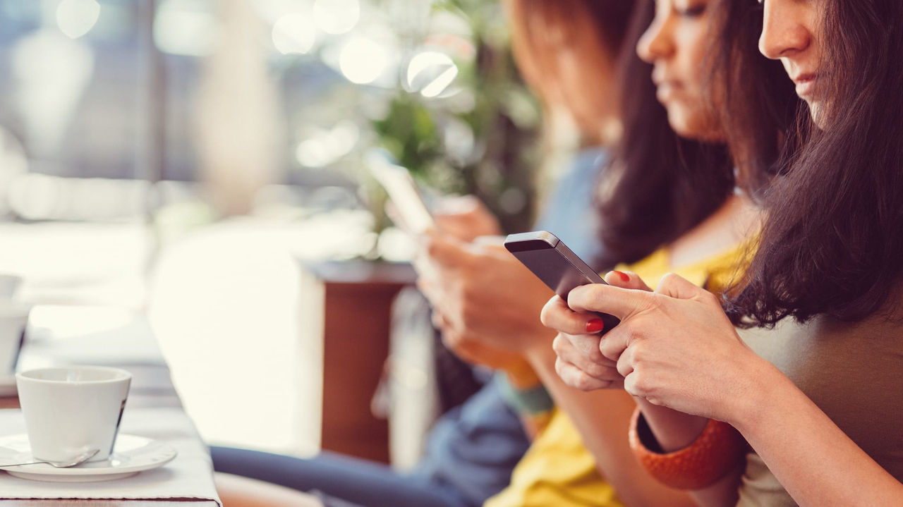 A group of women sitting at a table looking at their cell phones.