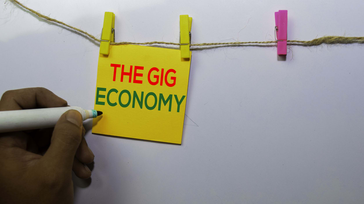 A person writing the word the gig economy on a piece of paper.