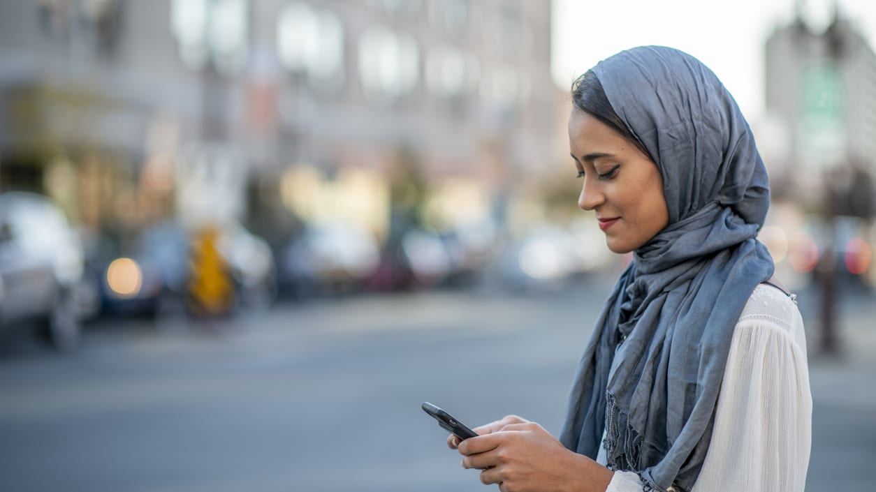A muslim woman looking at her phone in the street.